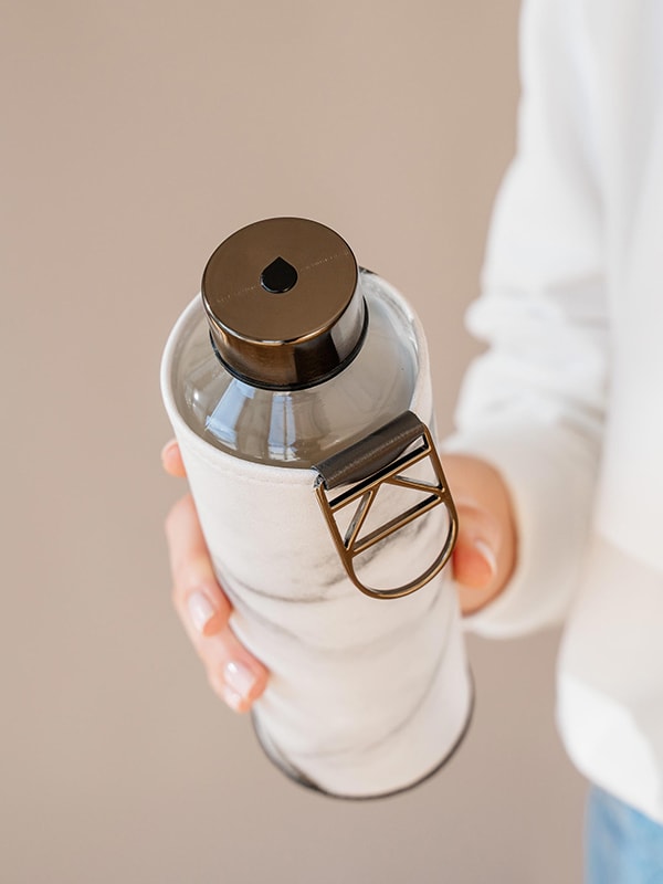 Stone Glass Water bottle from the top down, featuring the black metallic lid with drop logo and black metallic logo. In the background the black and white marble print on the glass water bottle cover.