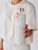 EQUA Sage reusable glass water bottle with white and grey faux leather cover and golden lid and metallic handle