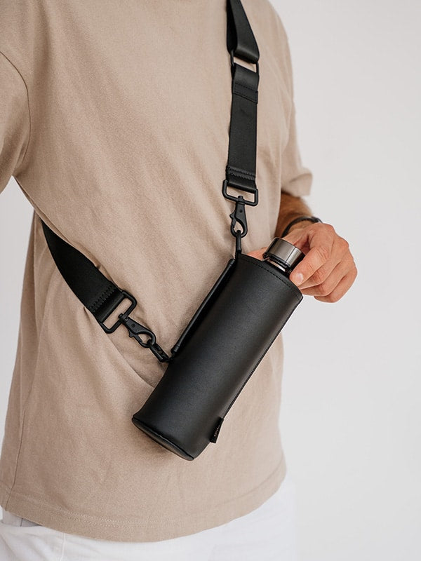 EQUA glass bottle in a faux leather bag with a long black strap to be carried crossbody.