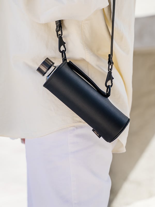 EQUA bouteille en verre dans un sac en faux cuir noir avec une longue lanière noire. 