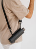 EQUA glass bottle in a faux leather bag with long strap, carried on the shoulder.