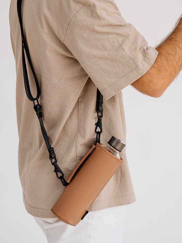 EQUA glass bottle in a brown faux leather bag with long strap carried on the shoulder. 