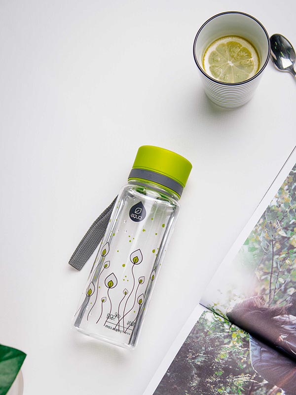 EQUA BPA BREZPLAČNA steklenica vode, Zeleni listje, steklenica vode na mizi skupaj z nekaj čaja in revijo, motiv listja, svetlo zelena in siva barva