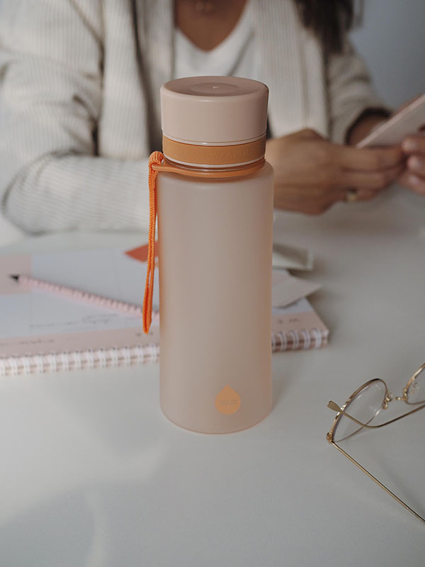 EQUA Botella de agua sin BPA, Amanecer, botella de agua en la mesa de la oficina, la mujer está trabajando en el fondo, diseño minimalista, sin motivo, color melocotón