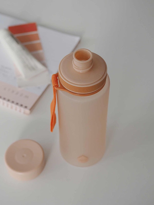 EQUA Botella de agua sin BPA, Sunrise, primer plano de la botella de agua sobre la mesa de la oficina, diseño minimalista, sin motivo, color melocotón