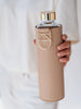 EQUA bouteille d'eau en verre Sienna dans les mains avec support et couvercle en or