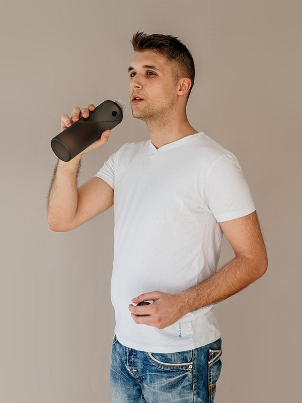 Uomo che beve da una bottiglia d'acqua nera, finitura opaca sulla bottiglia e logo a goccia, design minimalista Ashy water bottle by EQUA